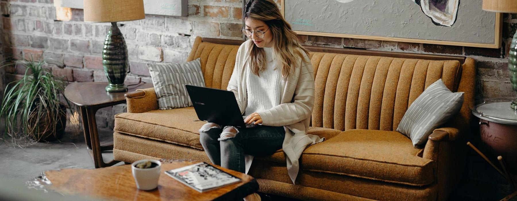 a woman sitting on a couch working on a laptop