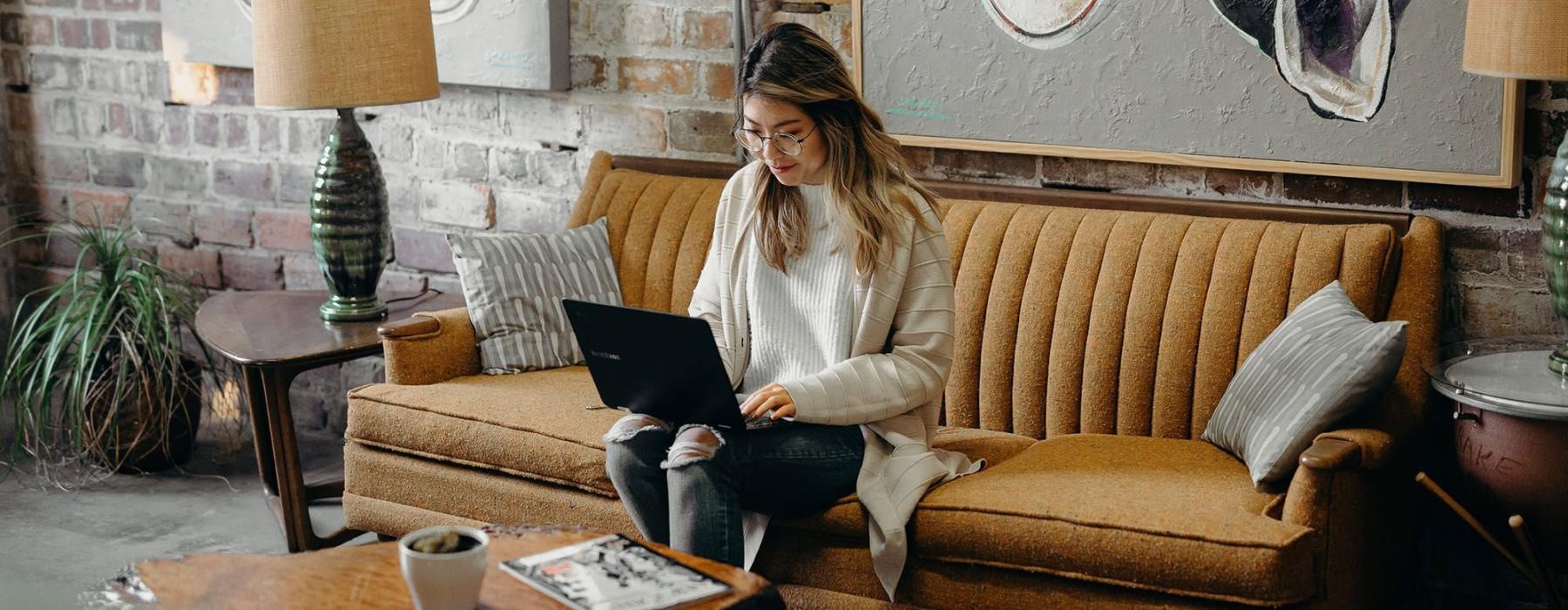 a woman sitting on a couch working on a laptop